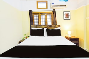 Une chambre d’hôtel avec un lit, une table de chevet, une lampe, une fenêtre avec des rideaux et un tableau encadré au mur.