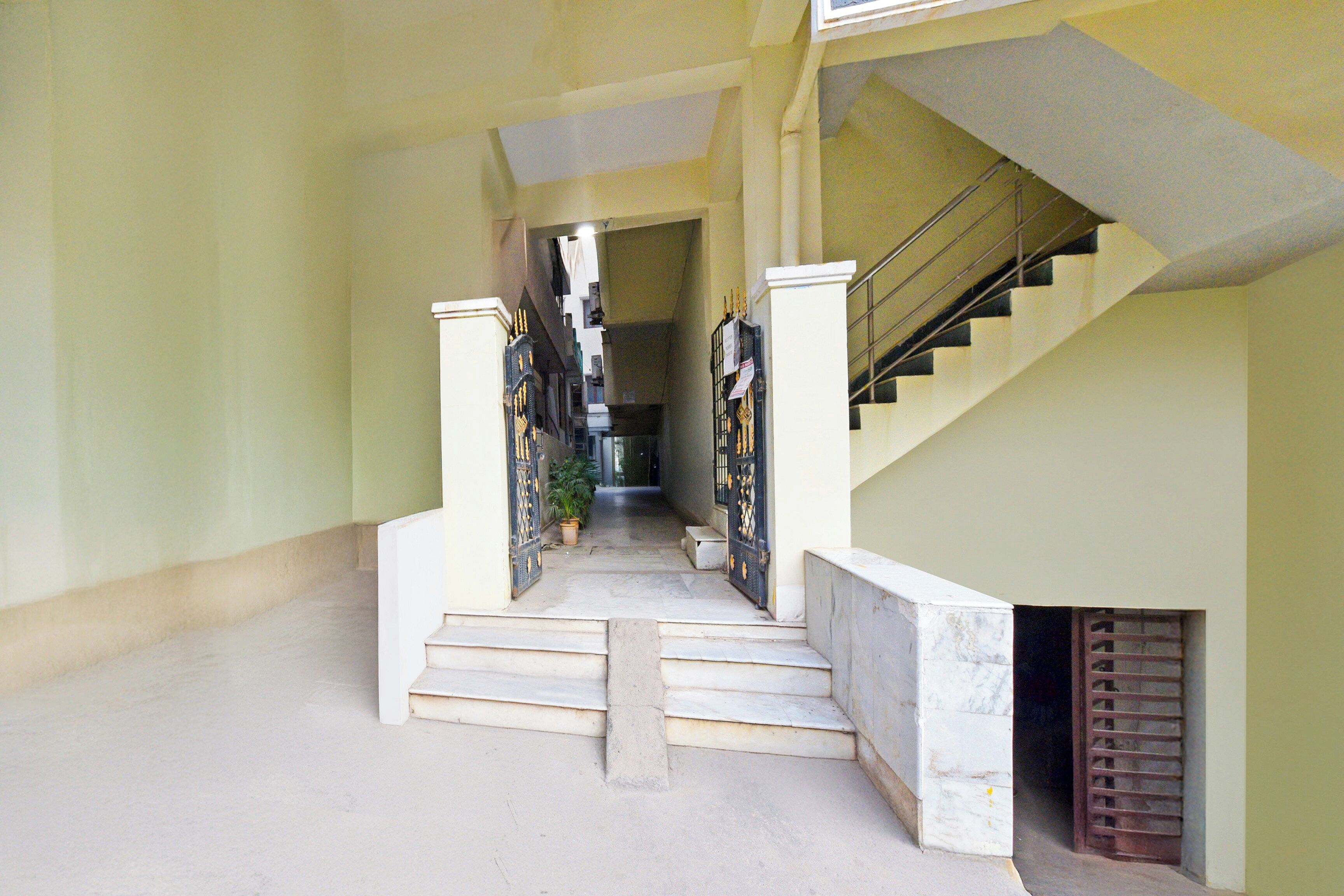 A corridor with a staircase leading to an upper level, a door with a metal gate, and a potted plant.