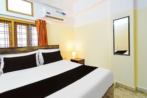 Une chambre d’hôtel comprenant un lit, une table de chevet avec une lampe, un appareil de climatisation, une fenêtre avec des rideaux et un miroir fixé au mur.
