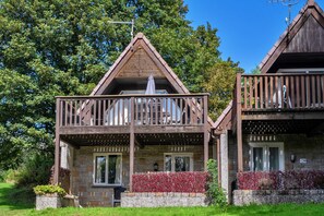 A two-story lodge with a balcony, stone facade, and a wooden roof.