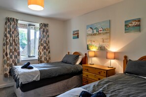 A bedroom with two beds, a wooden dresser, and a window with curtains.