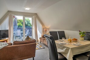 A dining area with a table set for two, a television, and a view of the outdoors.
