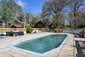 A rectangular swimming pool with a wooden deck surrounding it, a wooden fence, and a small shed in the background.