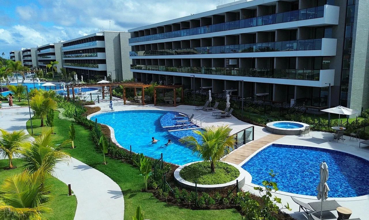 A hotel with multiple swimming pools, outdoor seating areas, and a modern building with balconies.