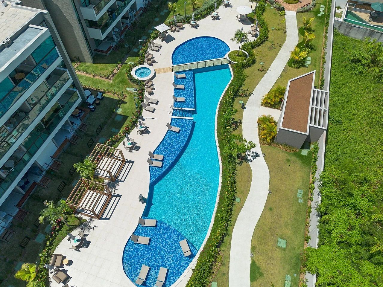 Vista aérea de um resort com uma grande piscina, áreas de estar e um jardim paisagístico.