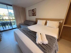 Habitación de hotel con cama, sofá, balcón con mesa y sillas, y dos cuadros en la pared.