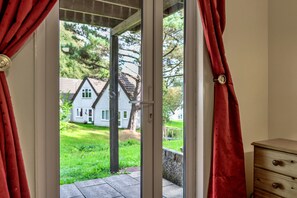 Une pièce dotée d’une porte-fenêtre coulissante donnant sur un jardin, d’une commode en bois et offrant une vue sur une maison blanche avec une pelouse verte.