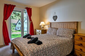 A bedroom with a bed, a nightstand, a lamp, and a window with curtains. - Daisy Valley Lodge (Callington)