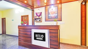 Mostrador de recepción de hotel con un cartel que indica servicio de empresa. Se observa un mostrador de madera, un cuadro enmarcado y un pequeño estante con objetos decorativos.