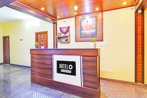 Ein Hotelrezeptionstresen mit einem Schild, das angibt, dass er firmenmäßig betreut wird. Es gibt einen Holztresen, ein gerahmtes Bild und eine kleine Ablage mit Dekorationen.