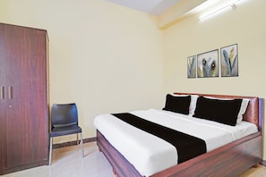 A bedroom with a bed, a wardrobe, a chair, and three wall-mounted paintings. - Hotel O Srigandhakavalu Formerly (Bengaluru)