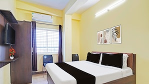 Habitación de hotel con cama, escritorio, silla, equipo de aire acondicionado y ventana con persianas.