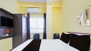 Habitación de hotel con cama, televisión de pantalla plana, ventana con cortinas y aire acondicionado instalado en la pared.