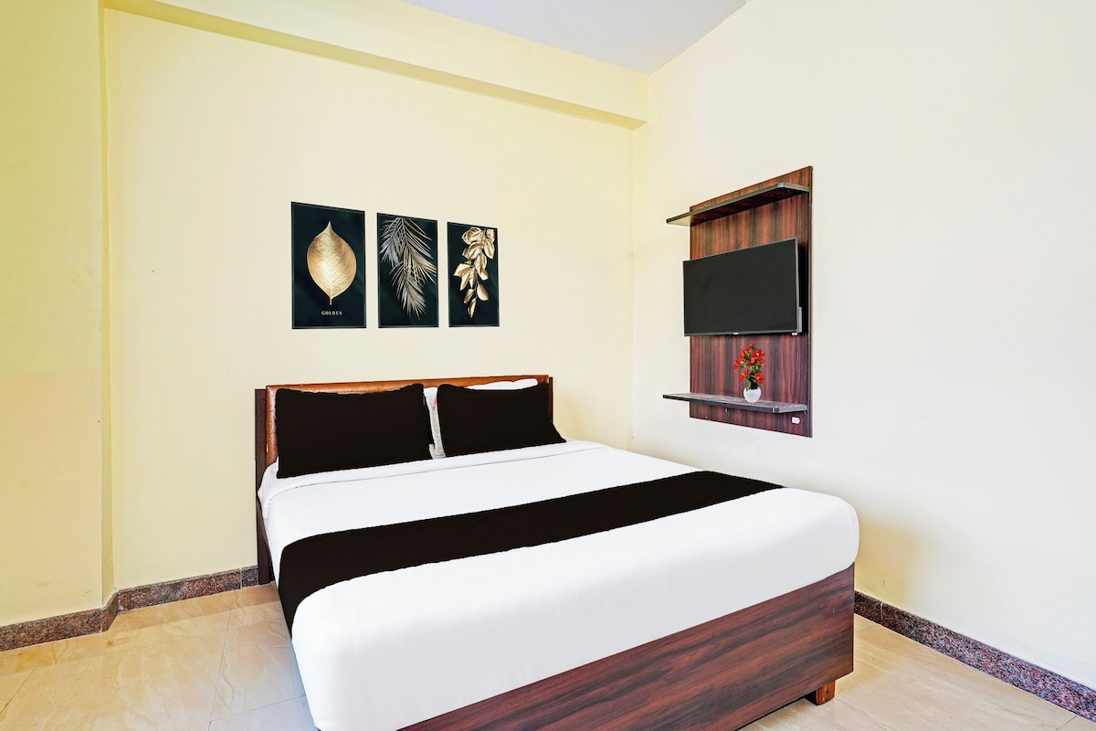 A hotel room with a bed, a flat-screen TV mounted on the wall, and three framed artworks on the wall.