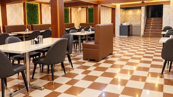 Uma área de refeições de hotel com piso xadrez, mesas, cadeiras e escada que leva ao andar superior.