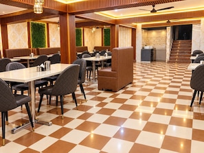 Uma área de refeições de hotel com piso xadrez, mesas, cadeiras e escada que leva ao andar superior.