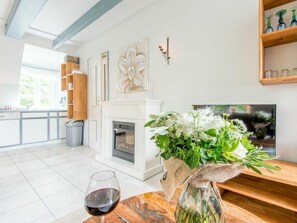 A modern living room with a fireplace, a dining table with a wine glass, and a kitchen area with white cabinets. - Holiday Apartment With 2 Bedrooms (Sylt)