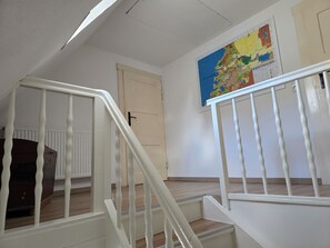Uma escadaria com corrimãos brancos que leva a um quarto com uma porta e um mapa na parede.