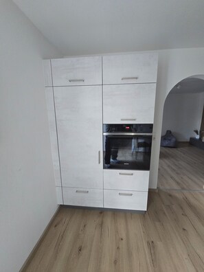 Cozinha moderna com armários brancos, forno embutido e piso de madeira.