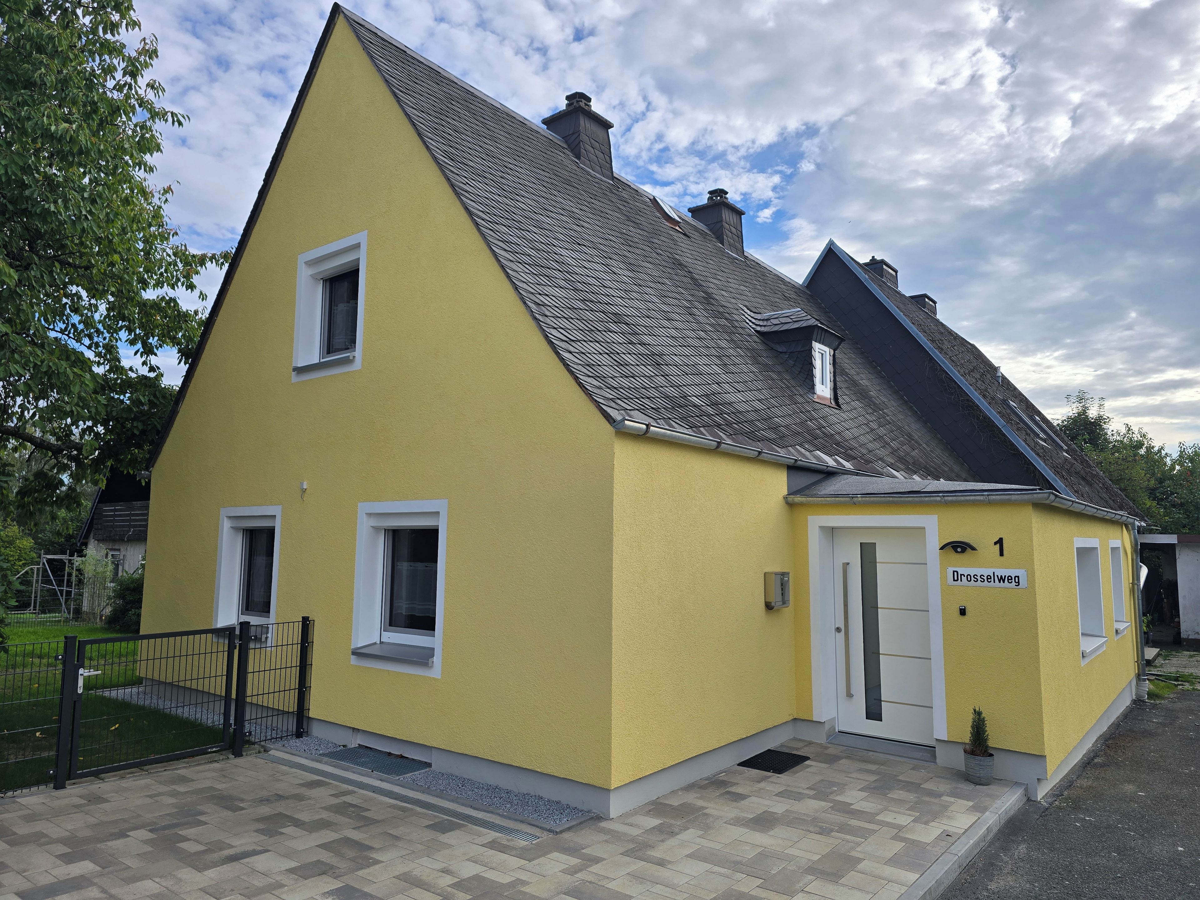Ein gelbes Gebäude mit Satteldach, einer weißen Tür und einem kleinen Fenster.