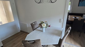En matplats med ett vitt bord, fyra stolar, en vas med blommor och en svart hänglampa.