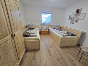 Quarto com duas camas de madeira, mesa de cabeceira, janela e guarda-roupa.