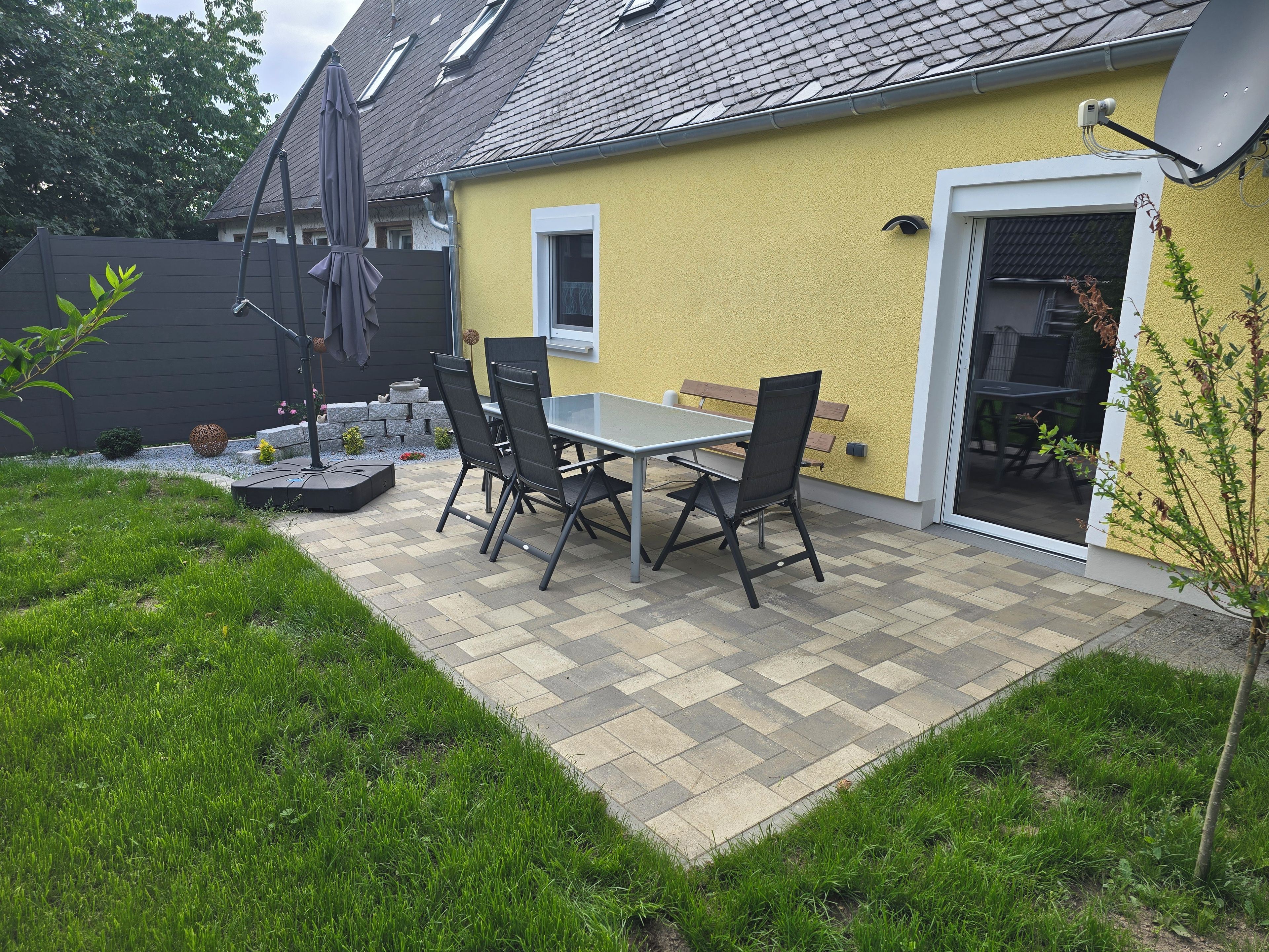 Eine Terrasse mit Tisch und Stühlen, eine Satellitenschüssel und eine Tür zu einem überdachten Bereich.
