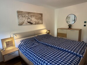 A bedroom with a bed, a nightstand, a dresser, a mirror, and a wall-mounted painting. - Bergzeit - One Bedroom Apartment in Kirchberg (Kirchberg in Tirol)