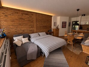 A modern bedroom with a large bed, a sofa, a dining table, and a kitchen area. - Bergzeit - One Bedroom Apartment in Kirchberg (Kirchberg in Tirol)