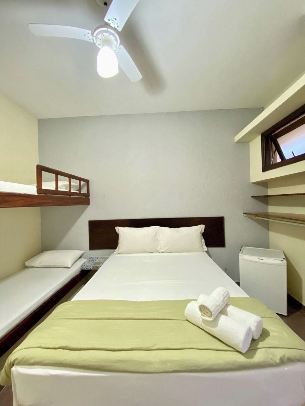 A hotel room with a single bed, a small bedside table, a ceiling fan, and a window.
