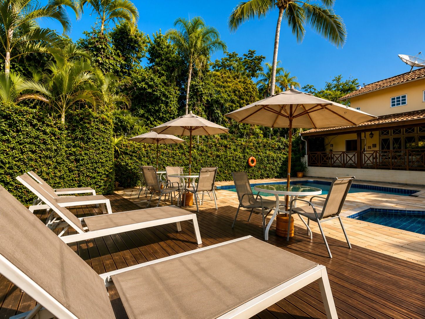 Zona de piscina con sillones, sombrillas y pileta.
