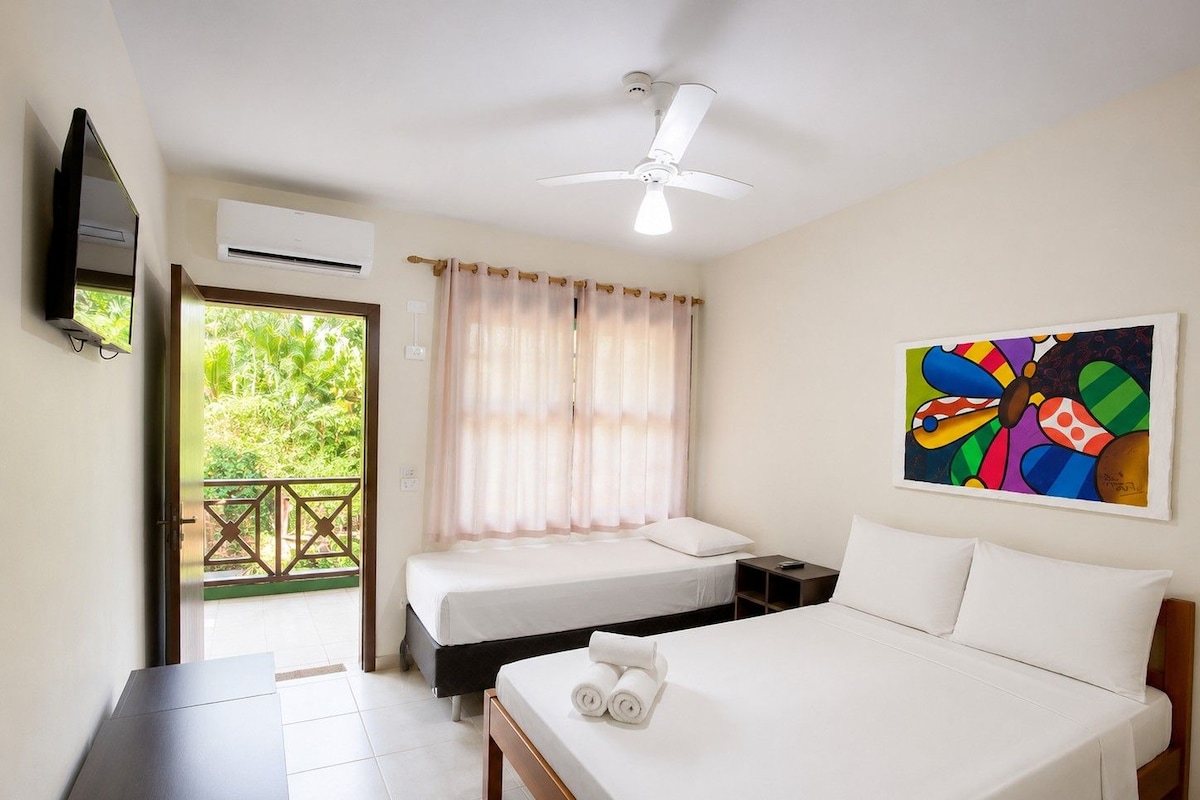 Une chambre d’hôtel avec deux lits, un ventilateur de plafond, un appareil de climatisation, un tableau et une vue sur la verdure environnante.