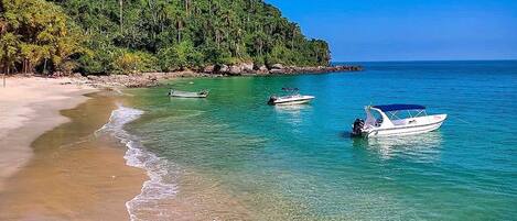 Una playa con agua turquesa cristalina, una orilla arenosa y una colina cubierta de bosque al fondo.