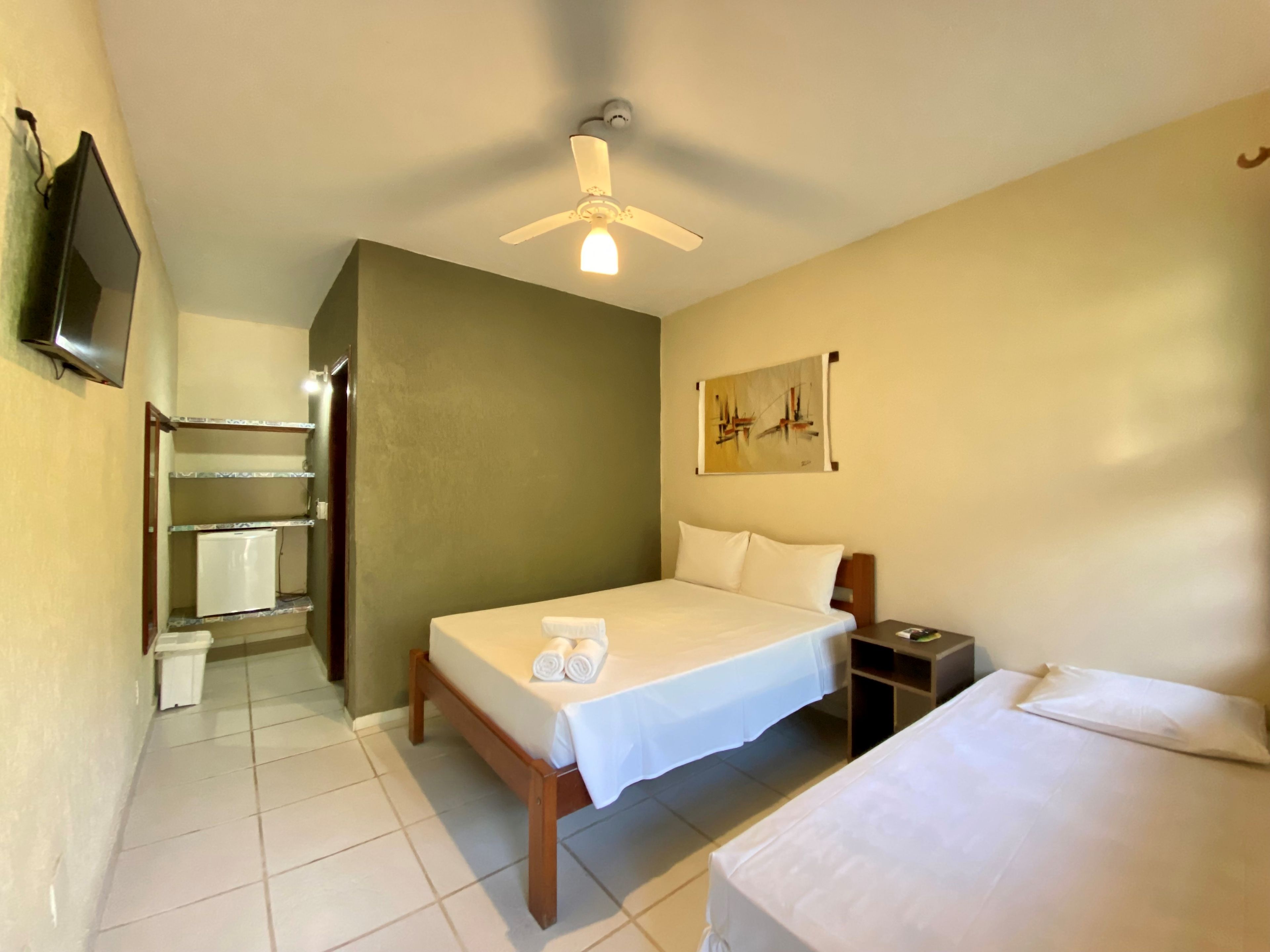 A hotel room with a bed, a nightstand, a wall-mounted TV, a ceiling fan, and a painting.