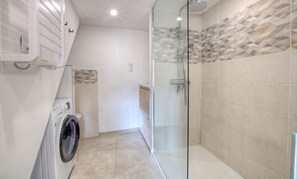 Un baño moderno con cabina de ducha de vidrio, lavadora integrada y suelo de baldosas.