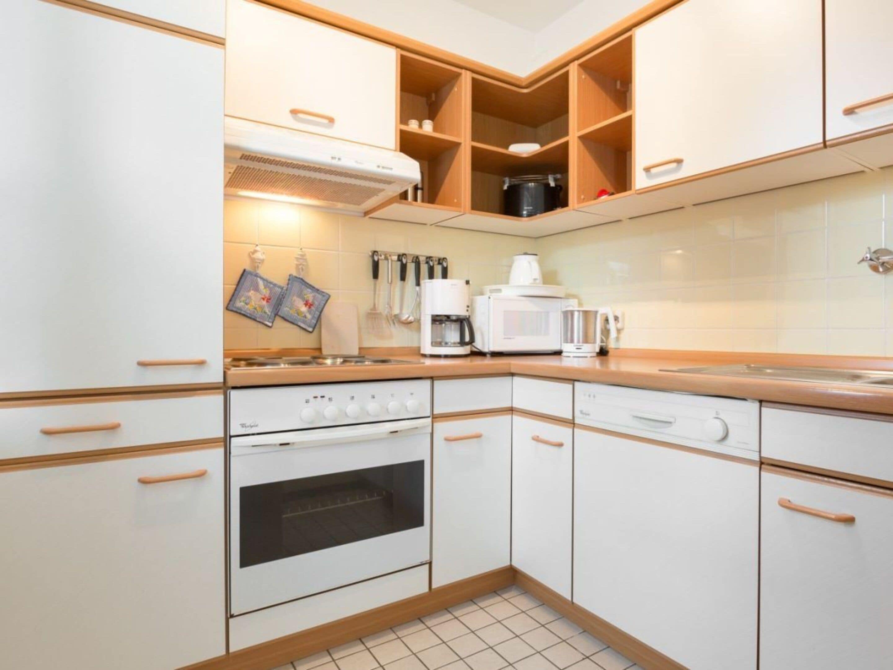 Cocina compacta con armarios blancos, estufa, horno y microondas.