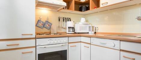 Cocina compacta con armarios blancos, estufa, horno y microondas.