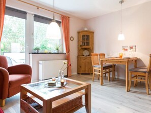 Ein gemütliches Zimmer mit Esstisch, Stühlen, einem Korbstuhl, einem Schrank und einem Fenster mit Vorhängen.