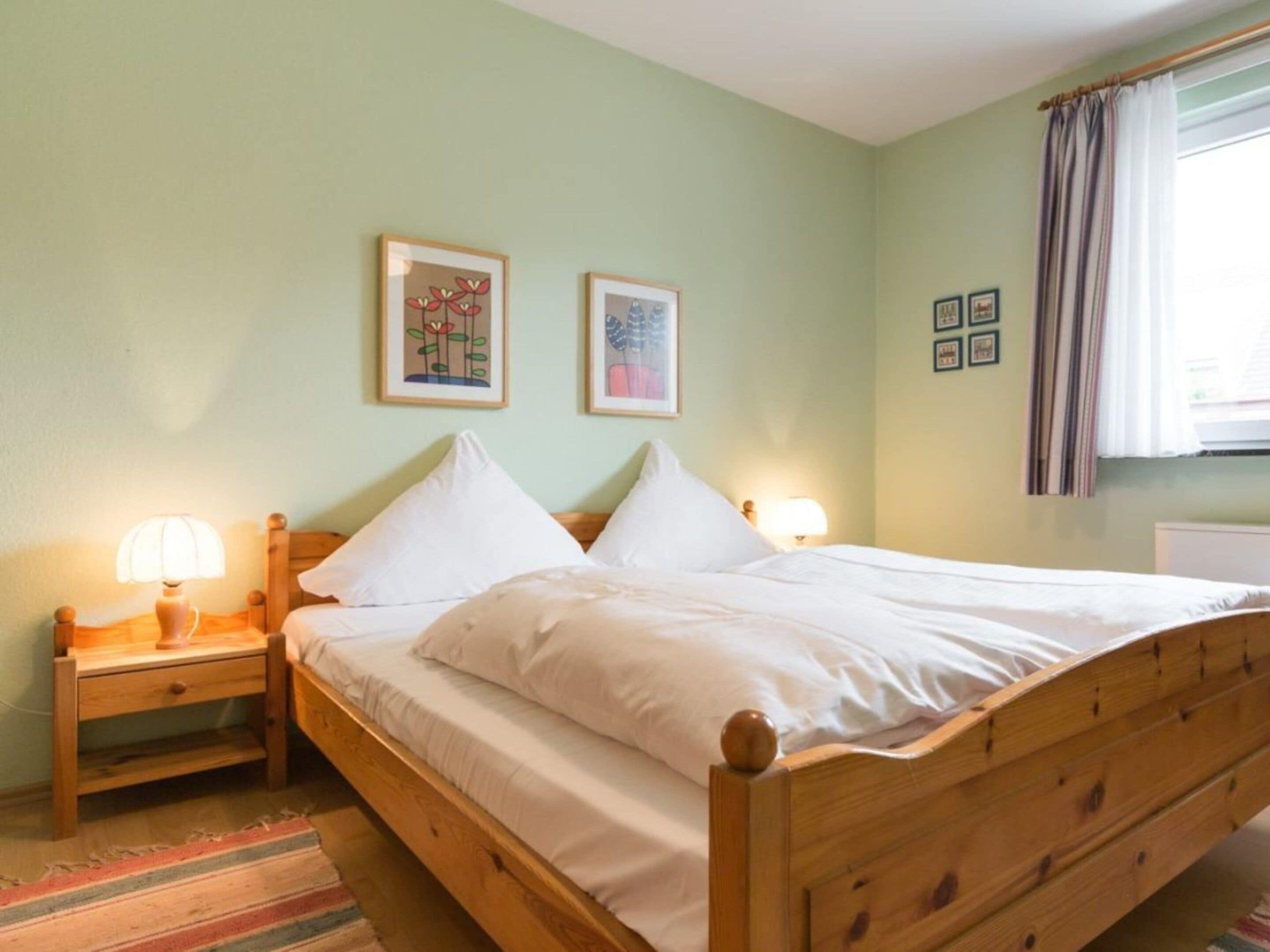 Cama de casal com cabeceira e peseira de madeira, duas luminárias de mesa e um tapete listrado.