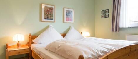 Cama de casal com cabeceira e peseira de madeira, duas luminárias de mesa e um tapete listrado.