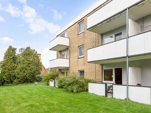 Ein mehrstöckiges Wohngebäude mit Balkonen, einem Rasen und einem großen Baum.