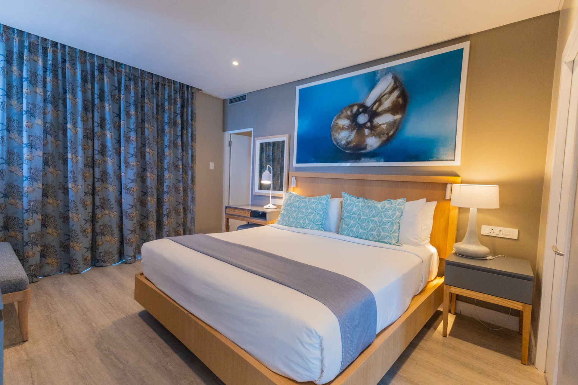 A hotel room with a large bed, a nightstand, a desk, and a painting on the wall.