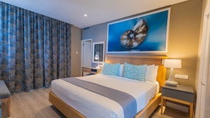 A hotel room with a large bed, a nightstand, a desk, and a painting on the wall. - Cabana Beach by First Private Stays (uMhlanga)