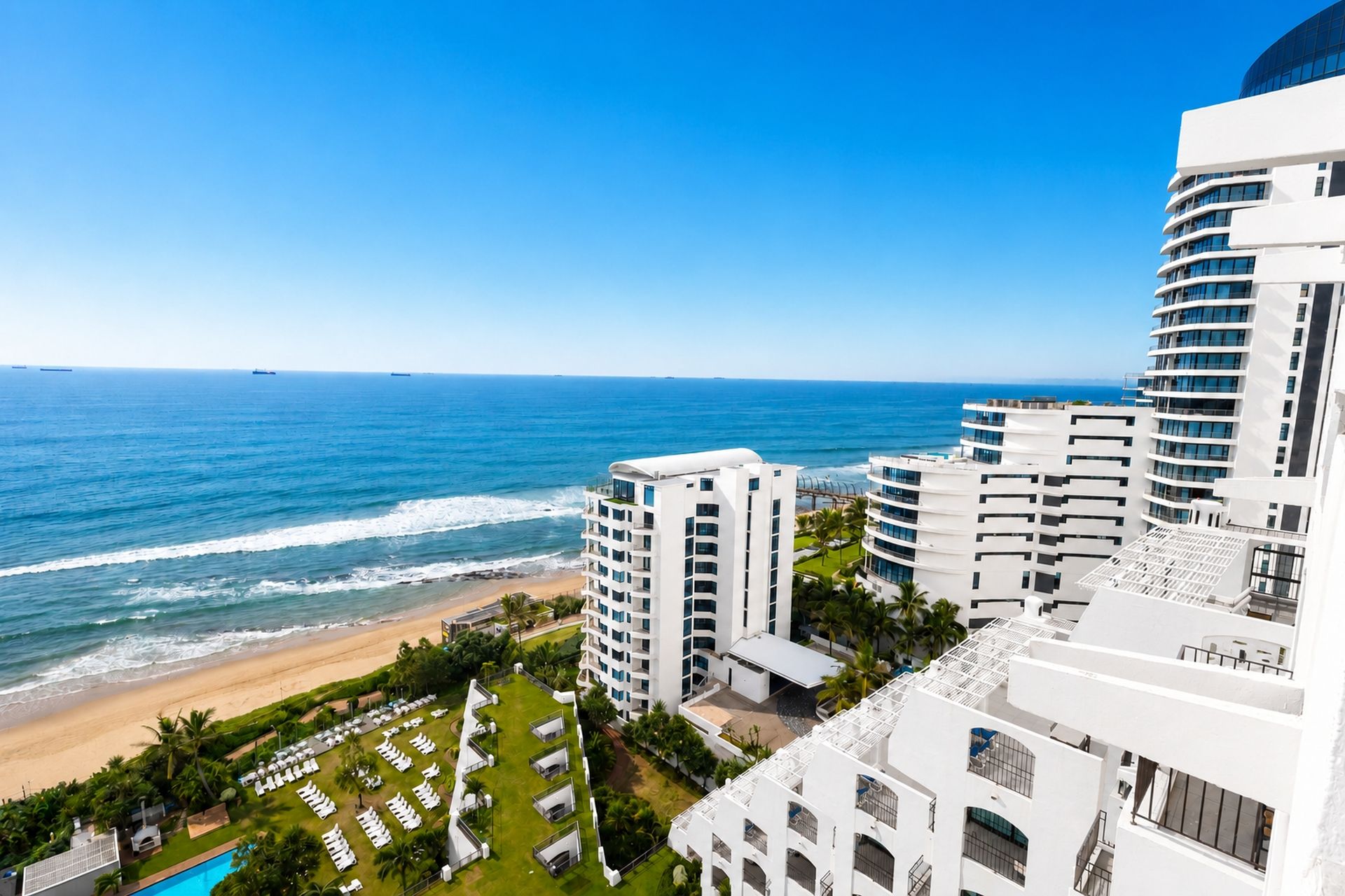 A beachfront hotel with multiple white buildings, a pool, and a view of the ocean.