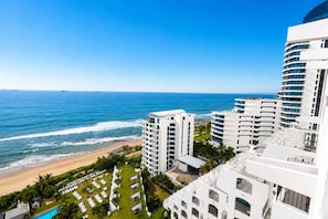 Um hotel à beira-mar com vários edifícios brancos, uma piscina e vista para o oceano.