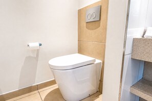 Un baño moderno con inodoro blanco, toallero y tirador de la cisterna en la pared.