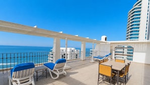 A sunlit outdoor seating area with a view of the sea, featuring white and blue lounge chairs and a table. - Cabana Beach by First Private Stays (uMhlanga)