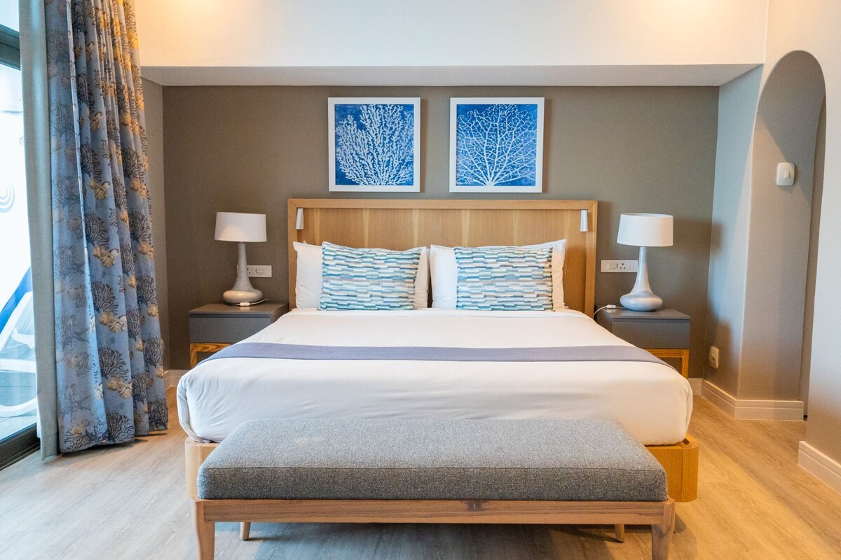 A hotel room with a large bed, two bedside tables, a bench, and two wall-mounted artworks.