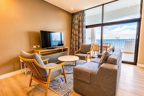 A modern hotel room with a television, seating area, and a balcony with a view.