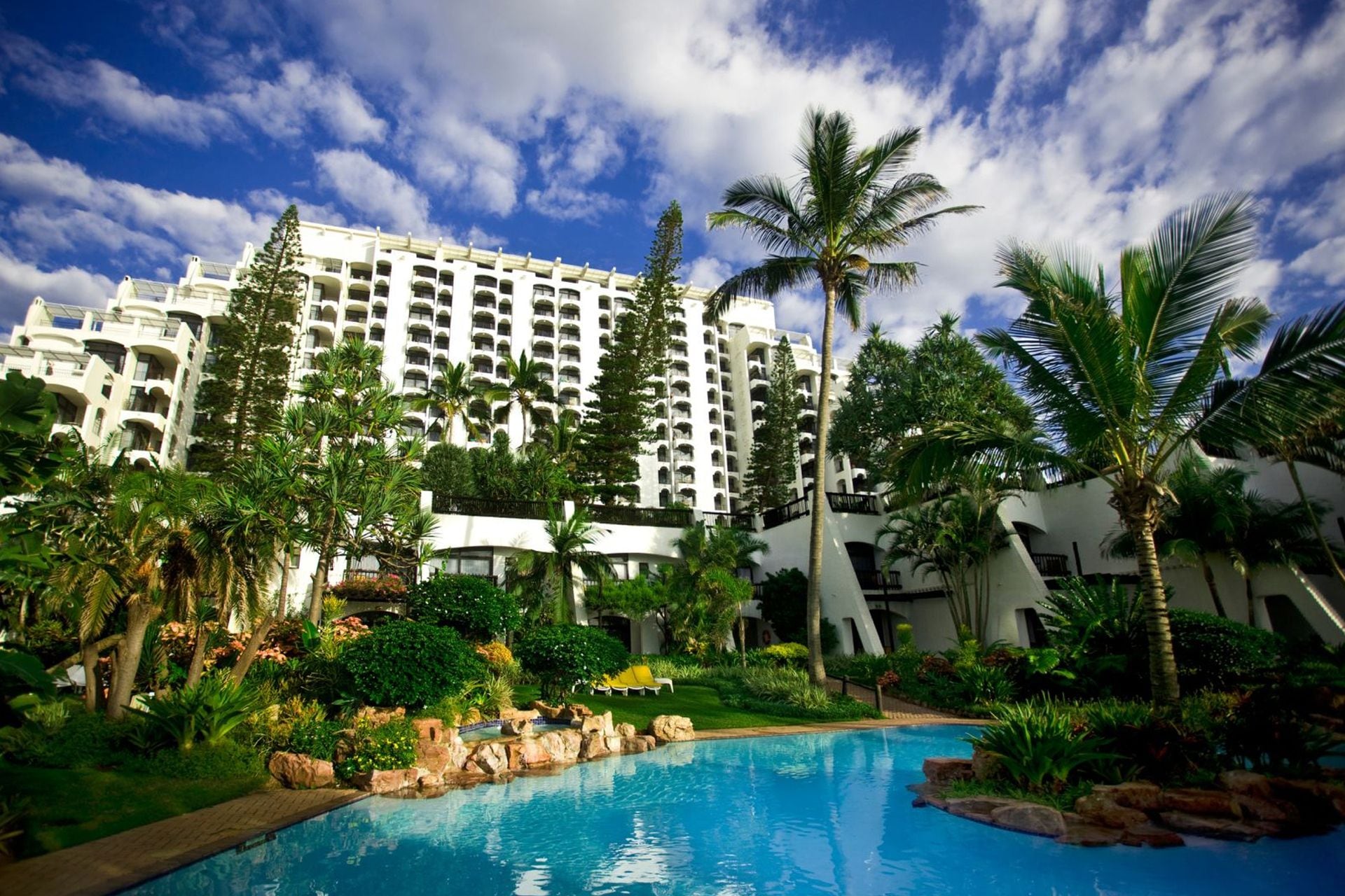 A hotel with a swimming pool surrounded by lush greenery and palm trees.
